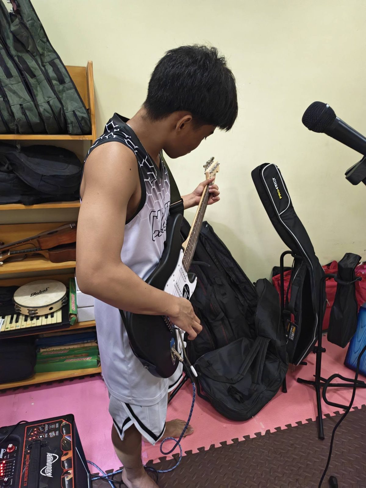 A young musician practicing electric guitar in the Kuya Center music room