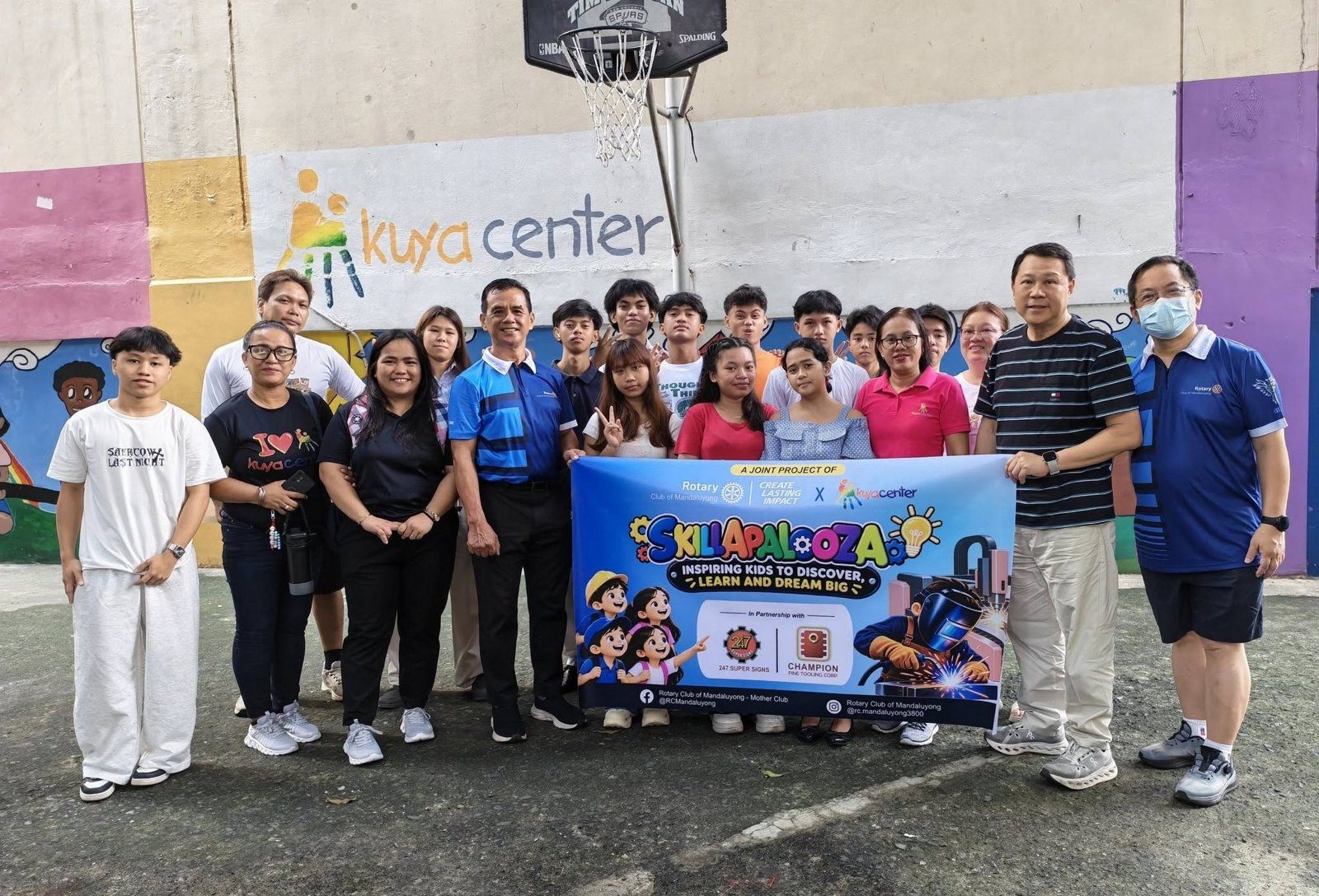 Kuya Center scholars, staff and Rotary Club of Mandaluyong members holding the Skillapalooza banner in front of the Kuya Center mural